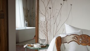A bedroom with a bed, a small table with a cup and cookies, and a view of a bathroom with a bathtub. - Marrucheti 82 (Campagnatico)