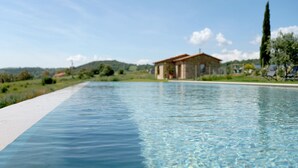 A clear swimming pool with a house in the background. - Marrucheti 82 (Campagnatico)