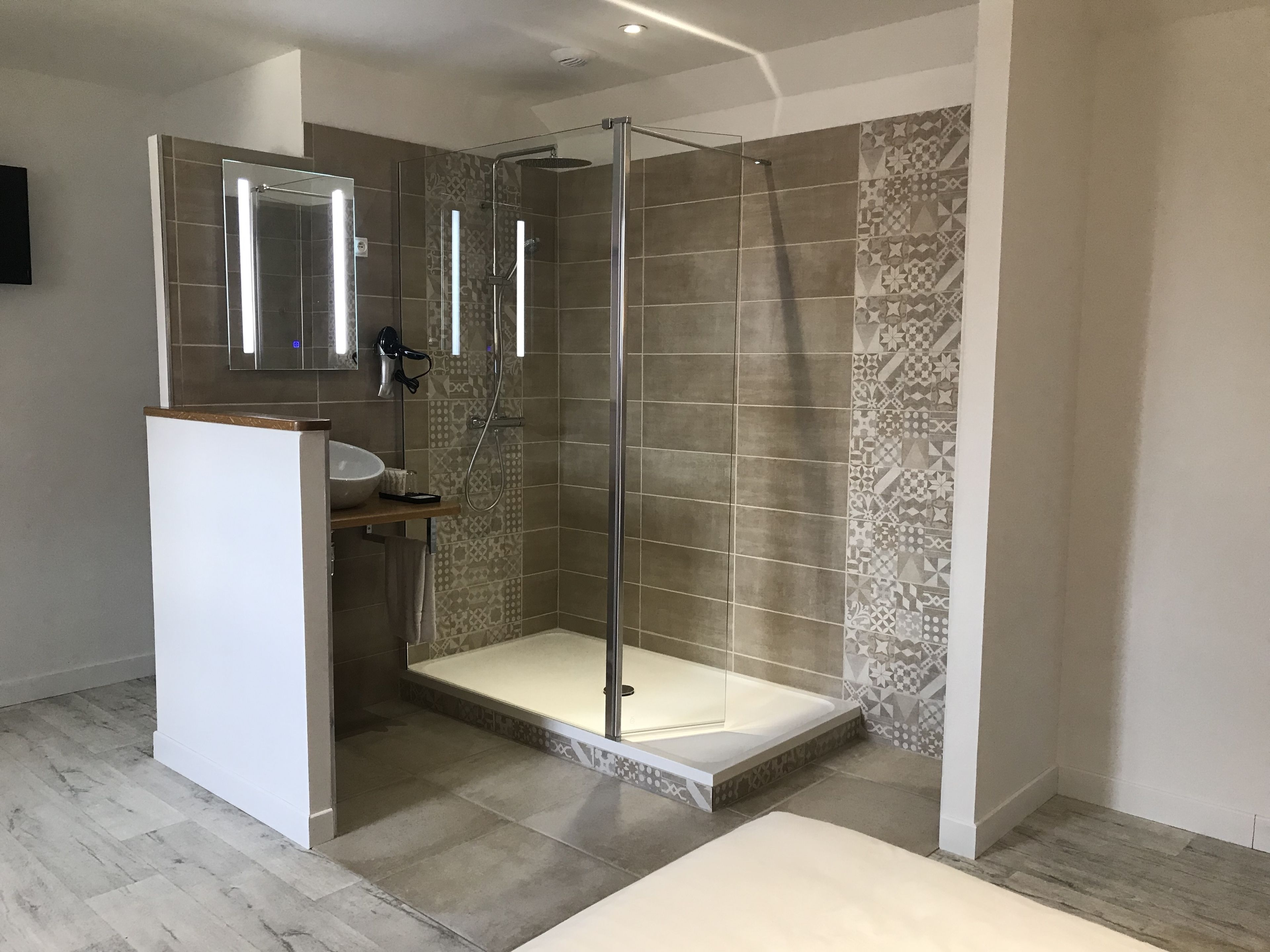 Un baño moderno con cabina de ducha de vidrio, tocador con lavabo y azulejos estampados.