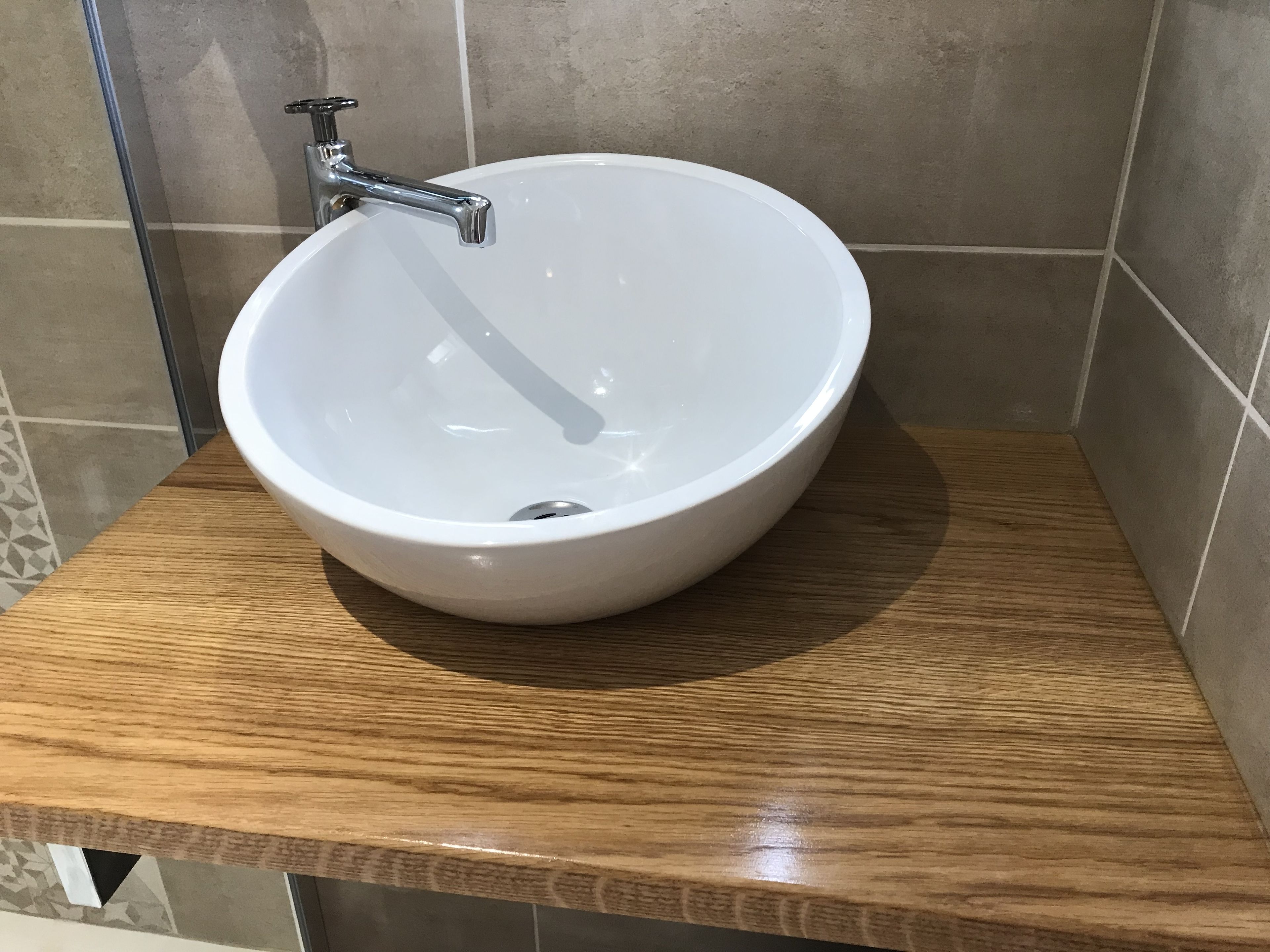 A white ceramic sink with a single faucet on a wooden countertop in a bathroom with tiled walls.