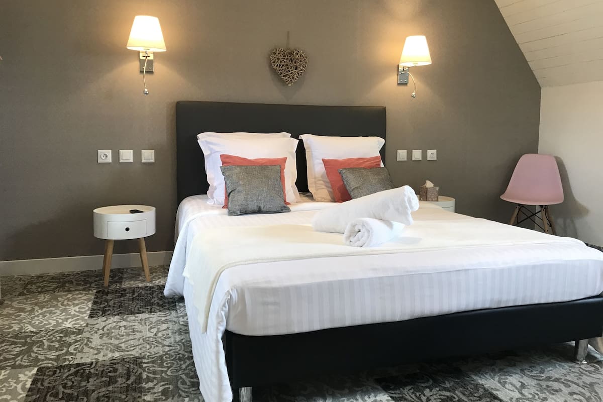 Ein ordentlich bezogenes Bett mit Kissen, ein Nachttisch, eine Lampe und ein Stuhl in einem Hotelzimmer.