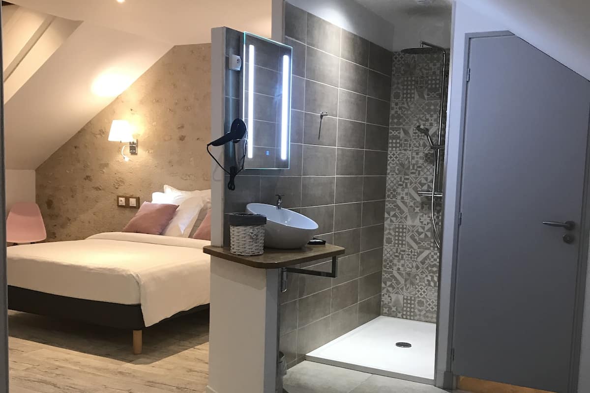 Ein Schlafzimmer mit Bett, Nachttisch, Spiegel und Duschbereich mit Glastür.