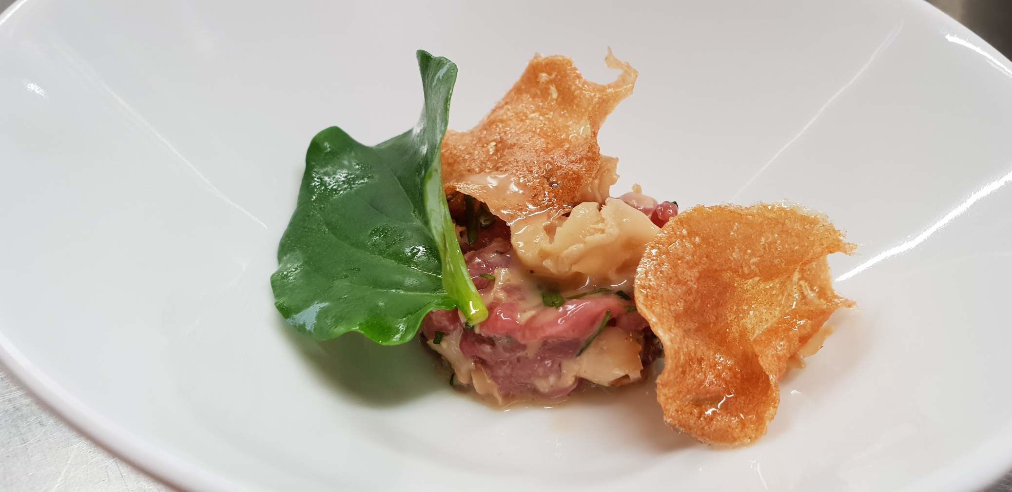 A white plate with a piece of food, possibly a sandwich or a folded pastry, accompanied by a green leaf.