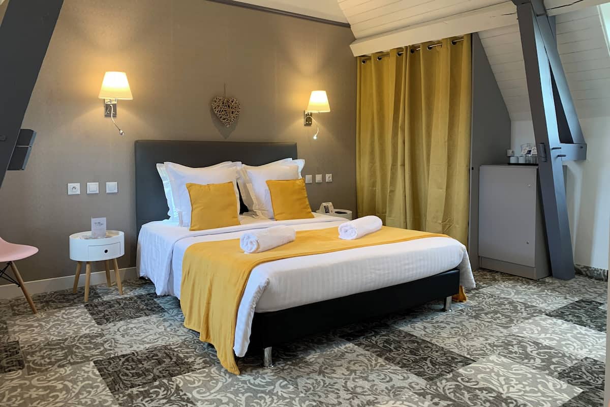 Ein Hotelzimmer mit einem großen Bett, zwei Nachttischlampen, einem kleinen weißen Tisch, einem Wanddekor und einer Minibar.