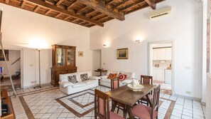 A spacious living area with a white sofa, a wooden dining table with chairs, a large cabinet, and a kitchen visible through an open doorway. - Rental In Rome Monti Apartment (Rome)