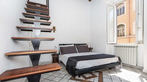 A bedroom with a bed, a wooden bench, a small table, and a staircase. - Rental In Rome Monti Apartment (Rome)