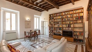 Un salon spacieux avec une grande bibliothèque, un coin repas comprenant des chaises, un canapé et un sol carrelé.