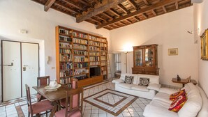 Un salon spacieux avec une grande bibliothèque, un ensemble de canapés, une table à manger avec des chaises et un plafond en bois.