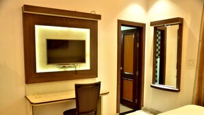 A hotel room with a TV mounted on the wall, a desk, a chair, and a bed. - Hotel Marc Royal (Agra)