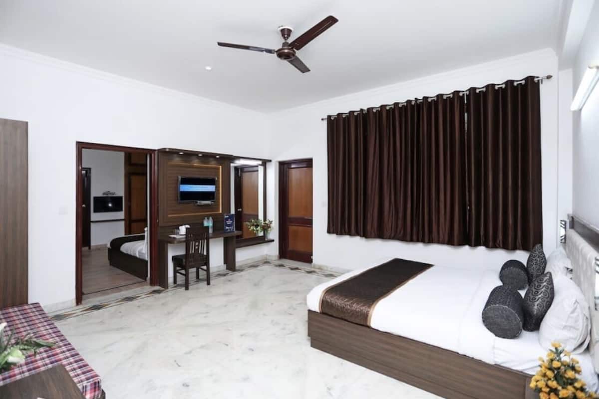 A hotel room with a bed, a desk, a chair, a ceiling fan, and a TV.