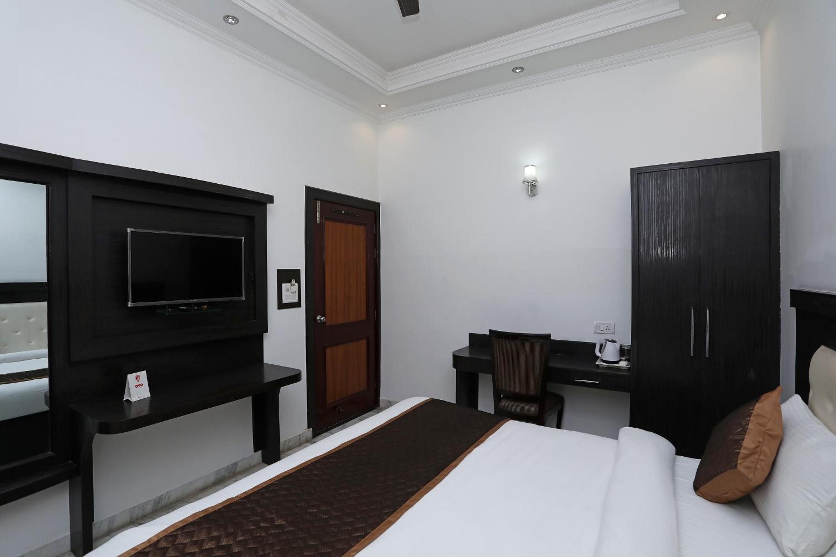 A hotel room with a bed, a desk, a television, a wardrobe, and a wall-mounted light.