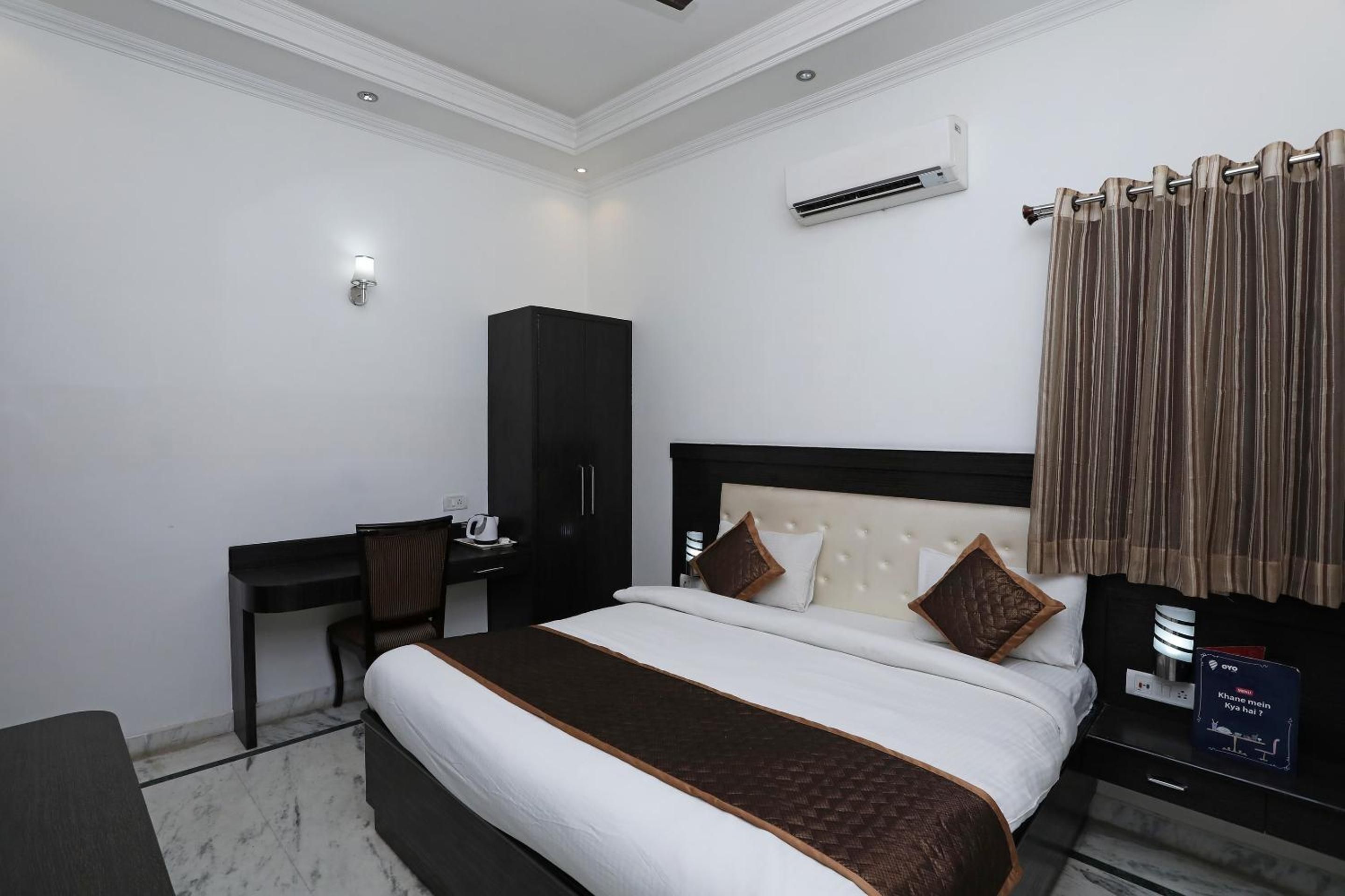 A hotel room with a bed, a desk, a wardrobe, and an air conditioning unit.