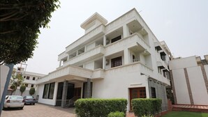 A multi-story residential building with a symmetrical facade, multiple balconies, and a well-maintained lawn. - Hotel Marc Royal (Agra)