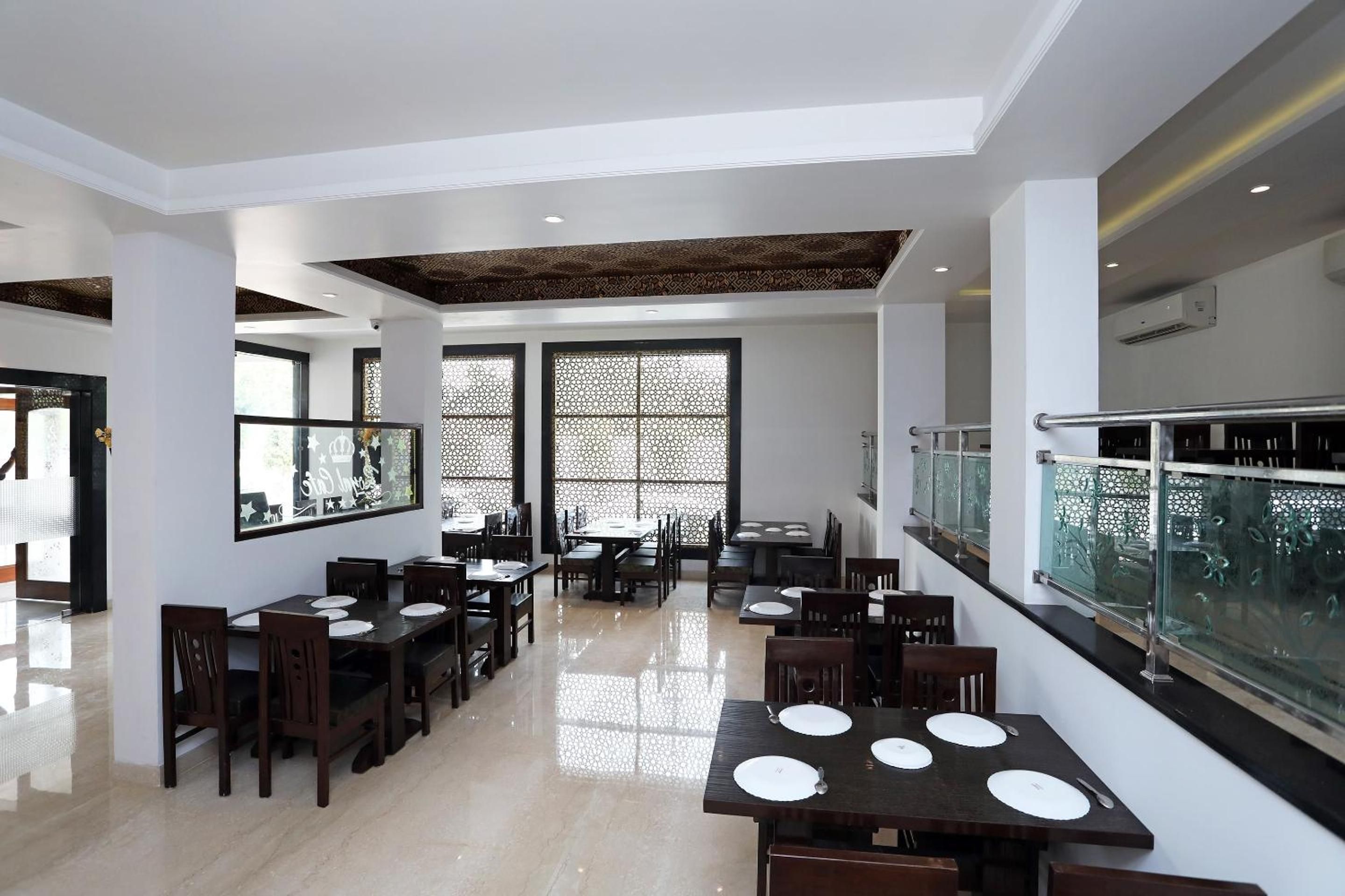 Un comedor amplio con varias mesas y sillas, un techo alto con vigas decorativas y ventanas grandes con celosías ornamentales.