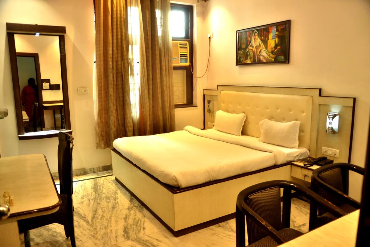 A hotel room with a large bed, a desk, a chair, a mirror, and a painting on the wall.