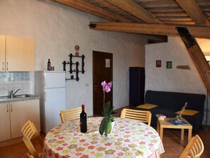 A cozy kitchen with a dining area, wooden ceiling beams, and a flower-patterned tablecloth.