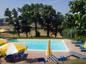 A swimming pool with lounge chairs and umbrellas, surrounded by trees and a view of the countryside.