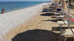 Una playa con tumbonas y sombrillas, cielo despejado y el mar al fondo.