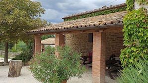 Un edificio rústico de piedra con tejado de tejas, un banco de madera y una planta en maceta al frente.