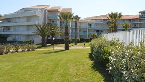Een meerlaags hotel met balkons, palmbomen en een omheinde tuin.