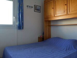 Ein Schlafzimmer mit einem Einzelbett, einem Holzschrank, einem kleinen Nachttisch mit einer Uhr und einem Fenster mit Vorhängen.