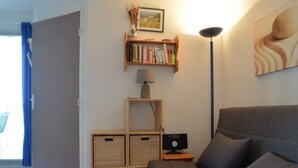 Een knusse woonkamer met een grijze bank, een boekenkast, een lamp en een aan de muur hangend schilderij.