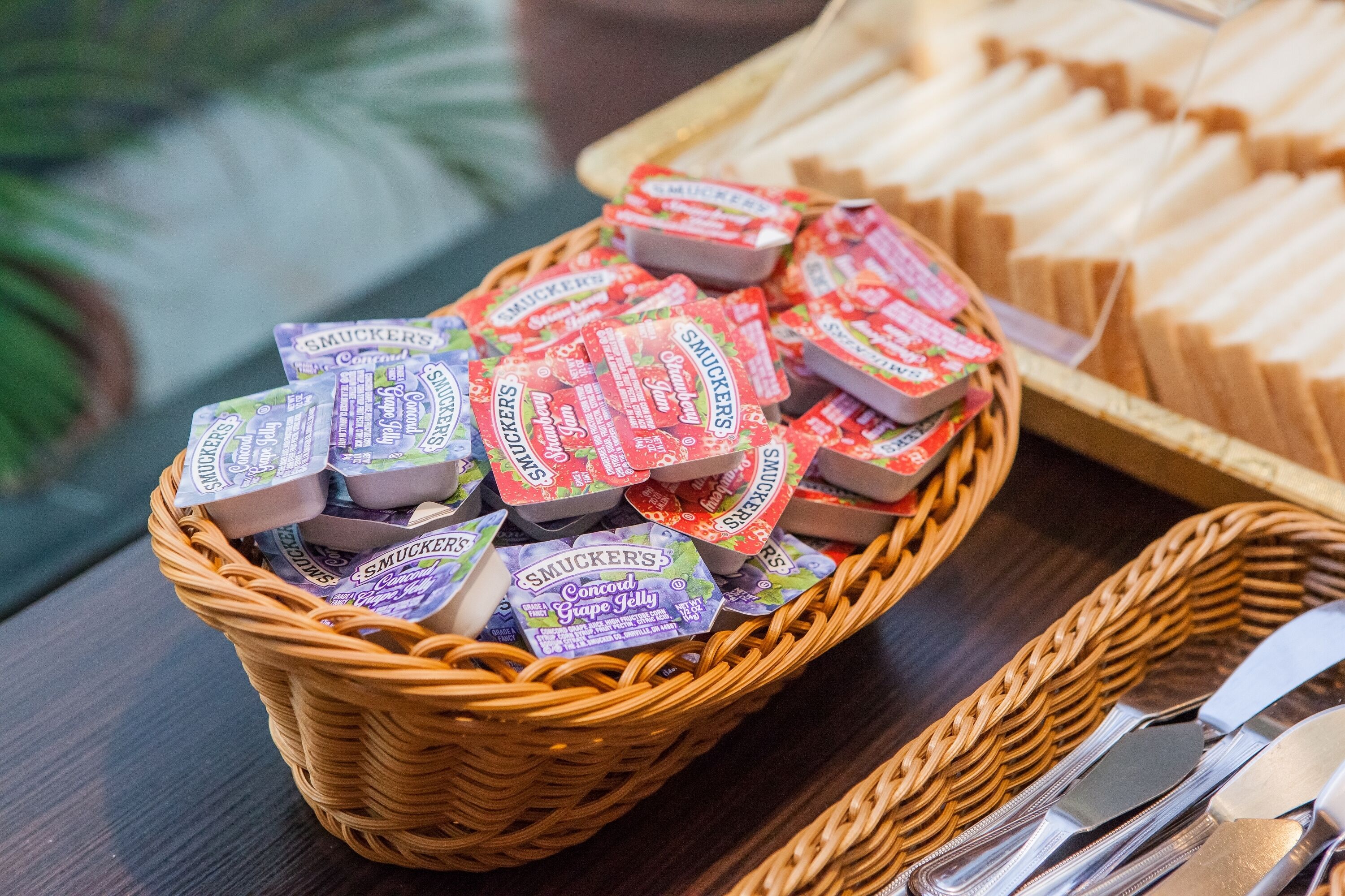 A basket filled with Smucker's Concord Grape Jelly packets on a wooden table.