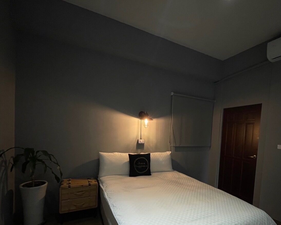 Een slaapkamer met een bed, nachtkastje, lamp, kamerplant en een houten kist.