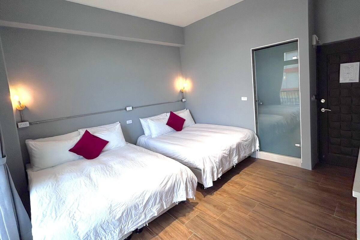 A hotel room with two beds, a wooden floor, and a door leading to a balcony.