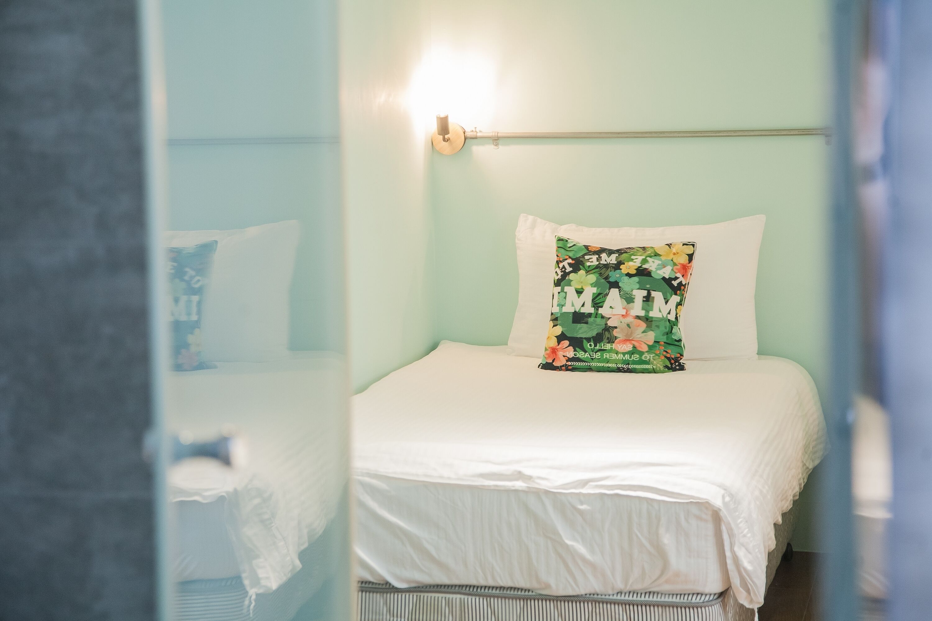 Una cama bien hecha con un cojín floral y una lámpara de pared.