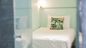 Una cama bien hecha con un cojín floral y una lámpara de pared.