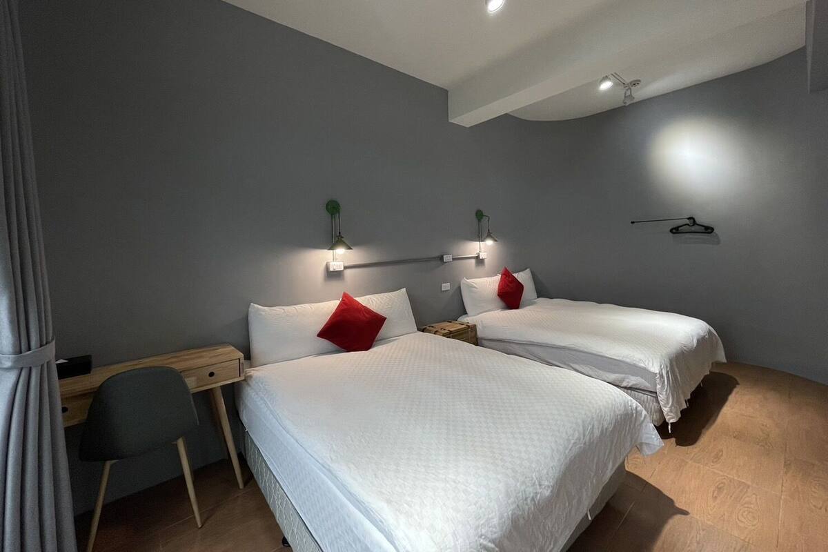 A modern hotel room with two beds, a desk, and a chair.