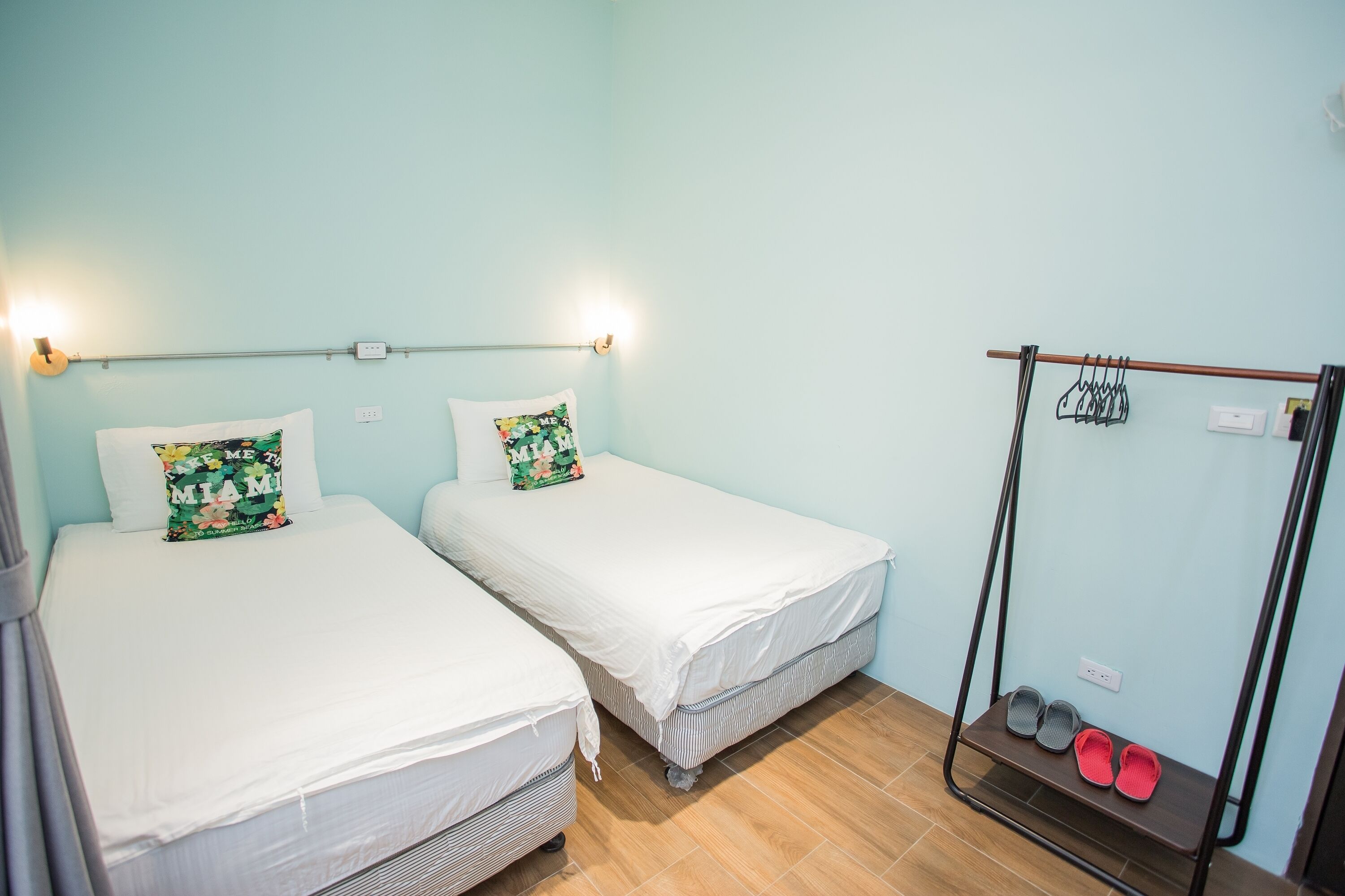 A room with two single beds, a small shelf with shoes, and a wall-mounted rack with hooks.