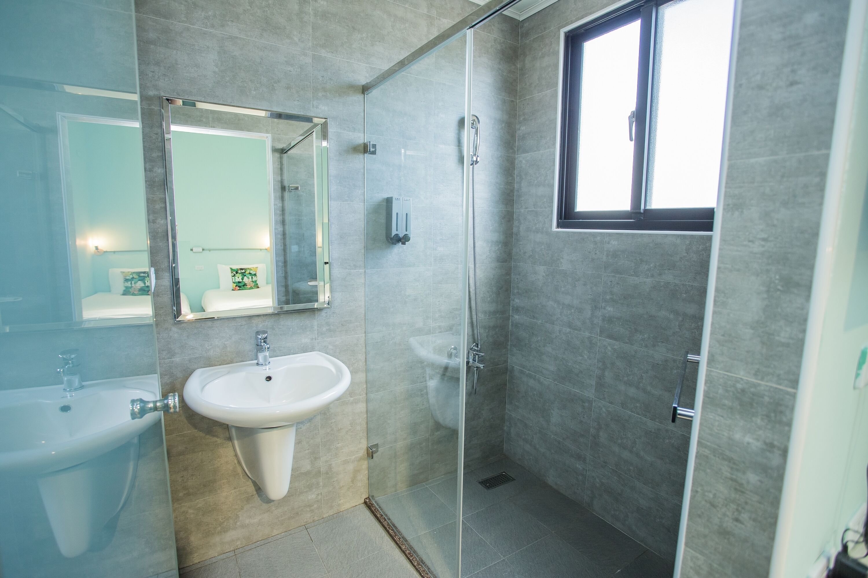 Un baño moderno con cabina de ducha de vidrio, lavamanos pedestal y un espejo grande.