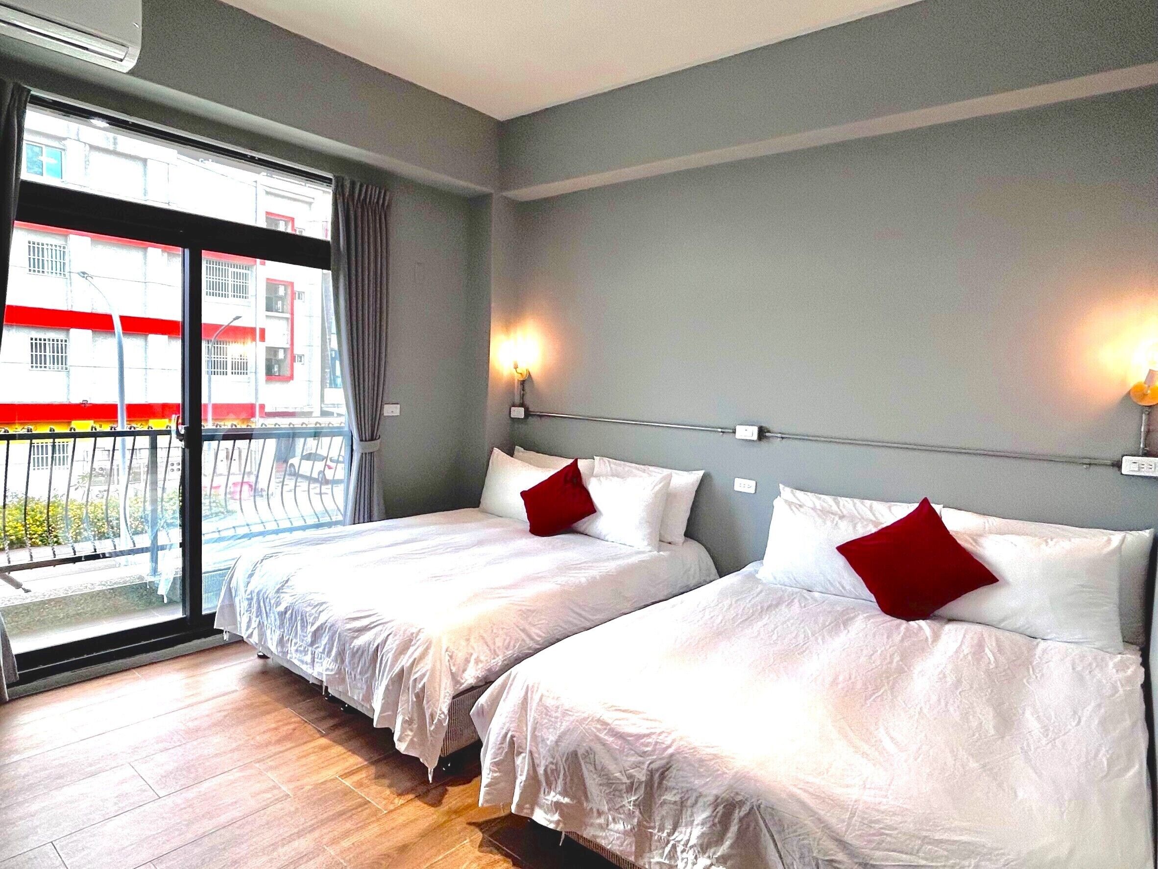 A hotel room with two beds, a balcony, and a view of buildings outside.
