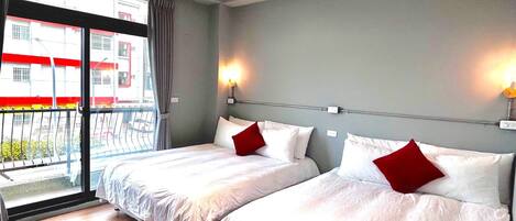 A hotel room with two beds, a balcony, and a view of buildings outside.