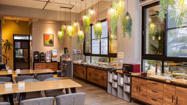A modern cafe with wooden tables and chairs, a buffet counter with various food items, hanging plants, and a large window providing natural light. - SunLight Forest (Taitung)