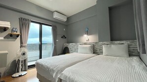 A hotel room with two beds, a fan, a window with curtains, a wall-mounted heater, and a view of the sea. - SunLight Forest (Taitung)