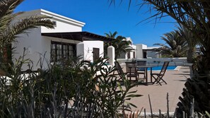 A poolside area with a white building, palm trees, and outdoor furniture.