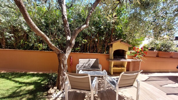 Un patio al aire libre con una mesa de madera y dos sillas, un horno de ladrillo pequeño y un calentador fijado a la pared.