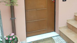 Una puerta marrón con manija de metal, un letrero de bienvenida y una pequeña maceta con flores rosadas y rojas.