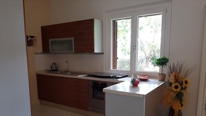 Una cocina moderna con microondas, estufa y lavaplatos. Se ve una ventana con vista a árboles y una planta en maceta sobre la encimera.