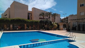 A swimming pool with a clear blue water feature, surrounded by a tiled deck and a low wall.