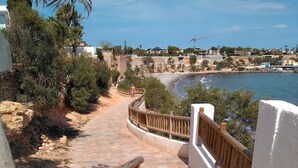 A stone staircase leading to a beach with a wooden railing, surrounded by greenery and buildings in the background.
