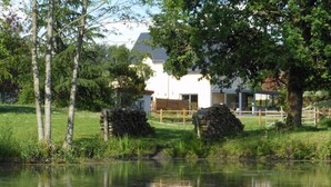 Un entorno tranquilo junto al lago con un edificio blanco al fondo, rodeado de árboles y una valla de madera.