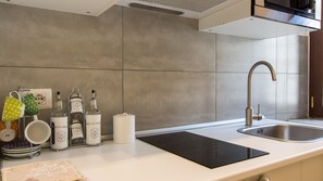 A modern kitchen with a stainless steel sink, a black induction cooktop, and a variety of kitchenware on the countertop. - Rental In Rome Pelliccia Apartment (Rome)