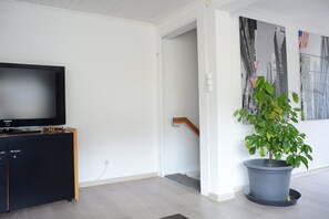 Ein Wohnzimmer mit Flachbildfernseher auf einer Kommode, einem Blumentopf und einer Treppe, die in einen anderen Raum führt.
