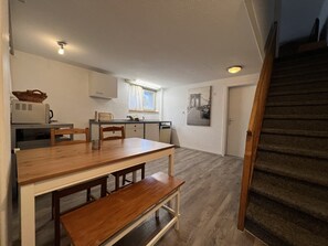Eine kleine Küche mit Esstisch, Stühlen und einer Bank. Eine Treppe ist rechts zu sehen.