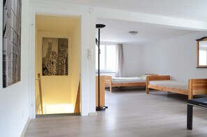 Ein Zimmer mit zwei Holzbetten, einer stehenden Lampe und einem gerahmten Stadtbild an der Wand.