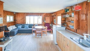 Ein gemütliches Blockhausszimmer mit einer Couch, Esstisch, Stühlen und einer Küchenzeile mit Holzausbau und Spüle.